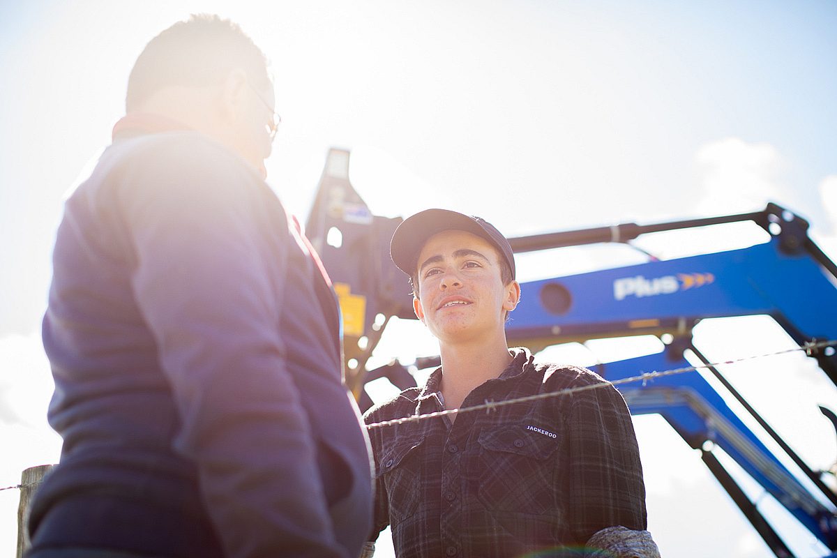 Young male agriculture apprentice talking to trainer beside heavy machinery