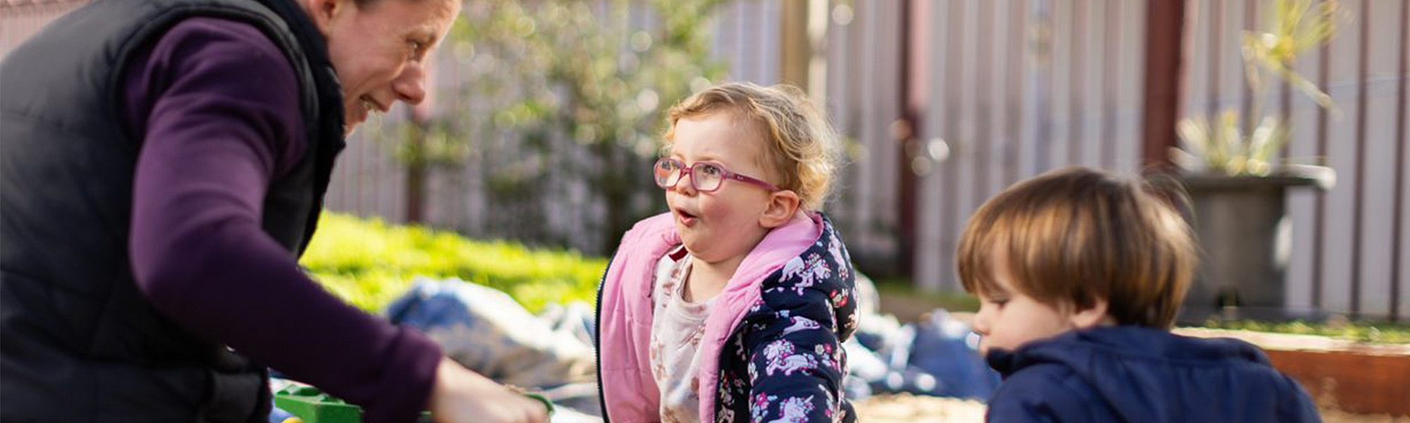 Mature age child care worker playing with kindergarten children in a sandpit