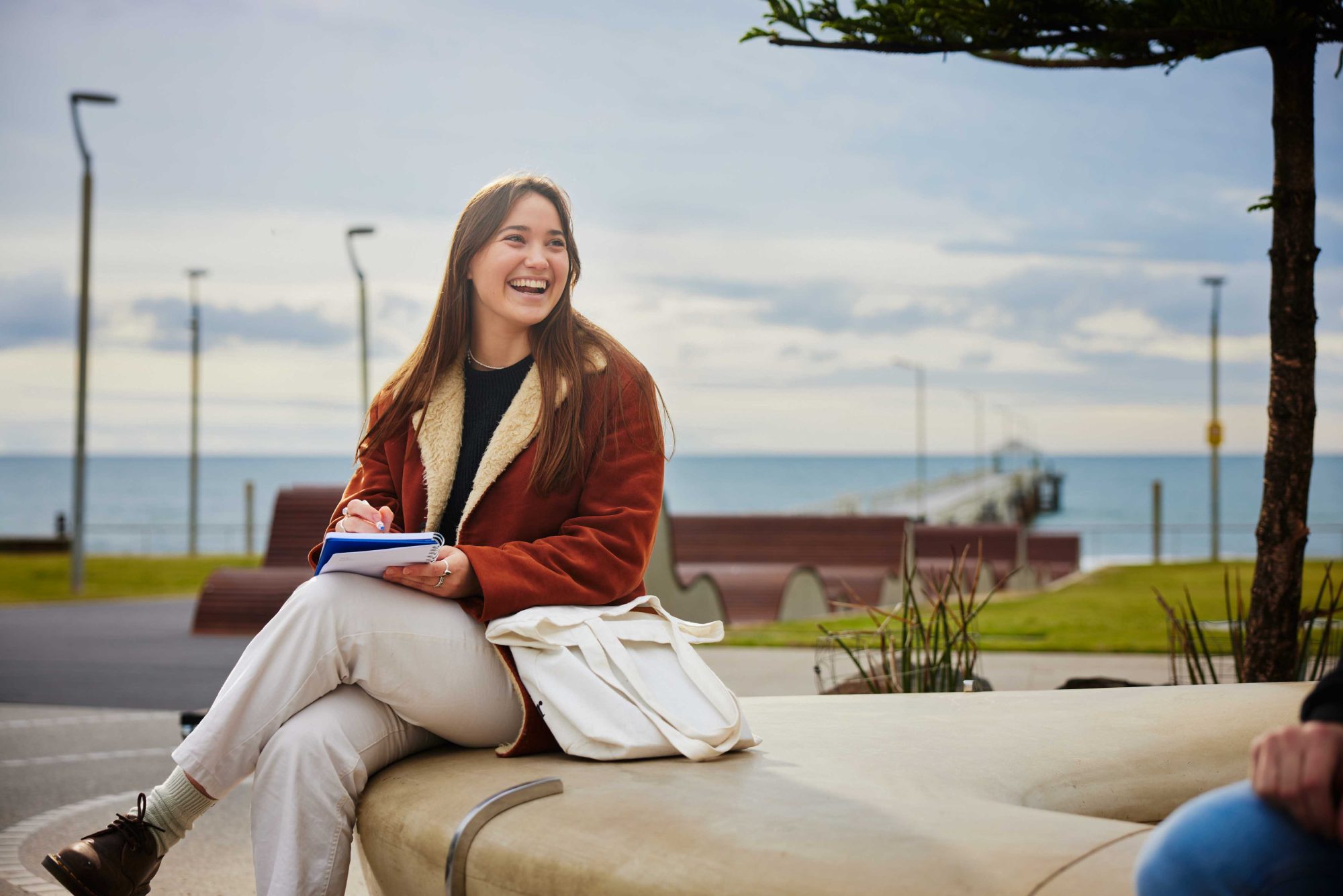 School leaver aged female talking to friend about VET study options on a bench by the sea