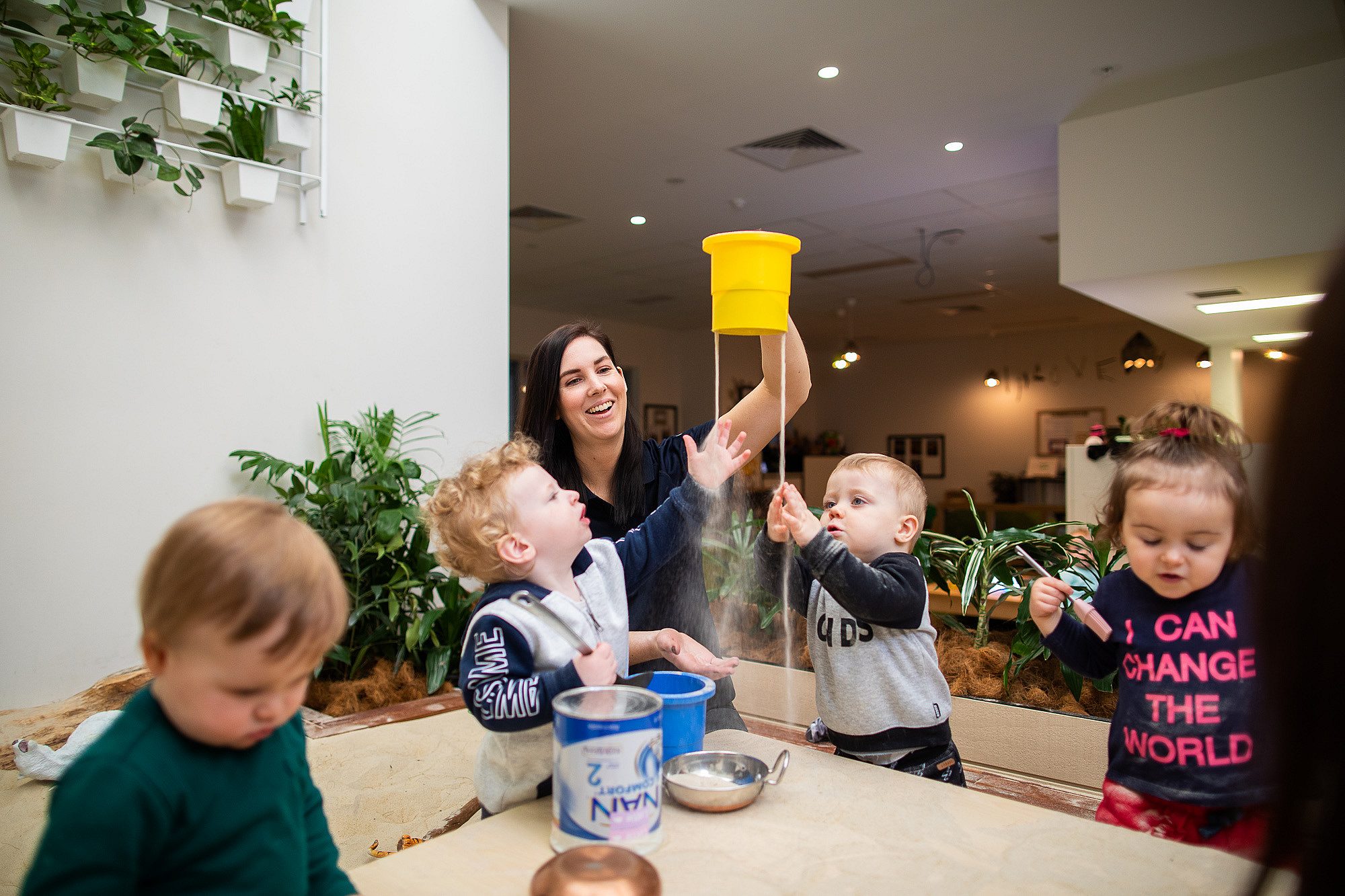 Childcare worker playing with sand with toddlers